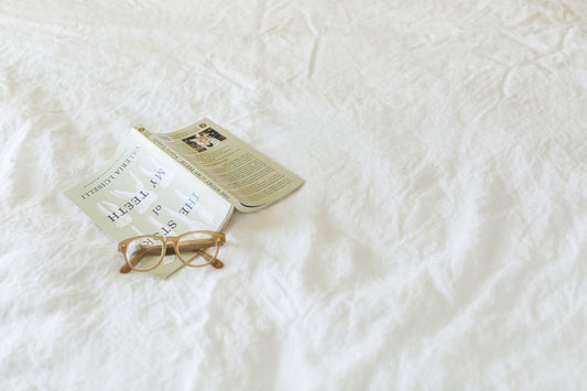 Book and glasses on bed as part of bedtime routine to build healthy sleep habits and improve sleep hygiene